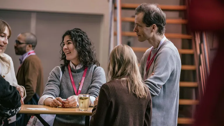 A man and three women are standing at a stand-up table chatting with each other.