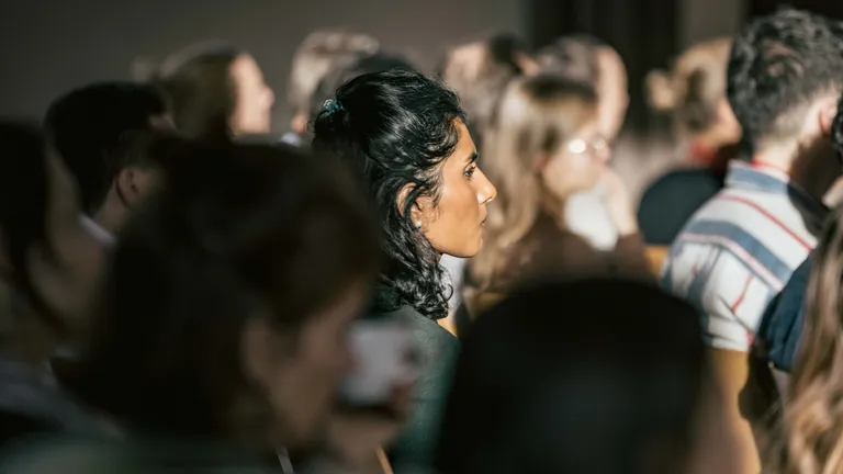 Side view of an audience that appears very dark; in the centre of the picture sits a woman illuminated by the sun.