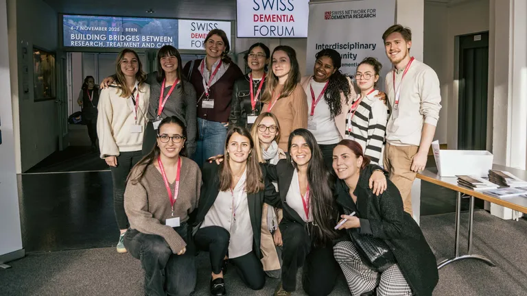 A group of young people, 12 women and one man, are crouching and standing in two rows for a group photo.