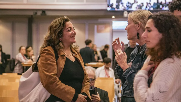 A room with tables and chairs arranged in a workshop setup. People are sitting on some of the chairs.