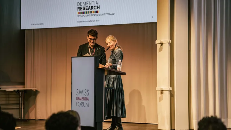 A woman stands behind the lectern on a stage with a man; she presents him with an award.